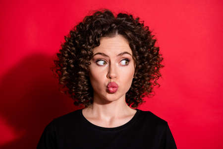 Close-up portrait of pretty charming flirty wavy-haired girl sending air kiss looking aside isolated over bright red color backgroundの写真素材