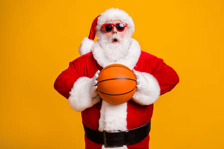 Portrait of his he nice attractive amazed wondered Santa holding in hands throwing orange ball team workout isolated over bright vivid shine vibrant yellow color backgroundの写真素材