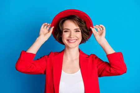 Close-up portrait of attractive cheerful lady wearing touching sunhat isolated over bright blue color backgroundの写真素材