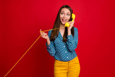 Portrait of lovely cheerful girlish girl talking handset receiver calling friend isolated on bright red color backgroundの写真素材