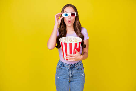 Portrait of lovely amazed wavy-haired girl wearing eyewear eating corn watching action thriller pout lip isolated bright yellow color backgroundの写真素材