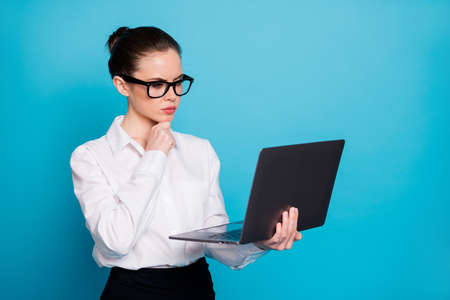 Close-up portrait of nice focused lady specialist holding in hands laptop browsing web reading isolated over bright blue color backgroundの写真素材