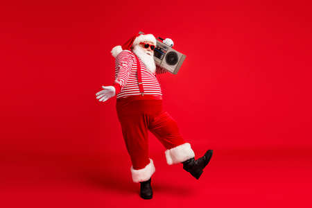 Full length body size view of his he handsome bearded fat overweight cheery Santa listening pop carrying tape player dancing having fun isolated bright vivid shine vibrant red color backgroundの写真素材