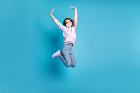 Full body photo of crazy excited girl jump raise hands wear white face mask isolated over blue...