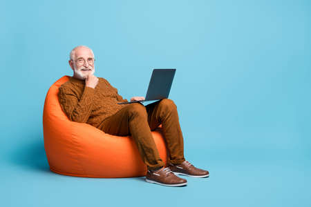 Portrait of bearded grey-haired man sitting in bag chair using laptopの写真素材