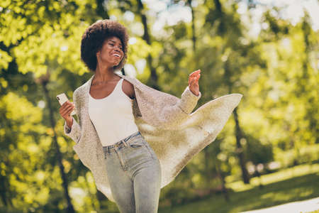 Photo of positive charming dark skin lady hold smartphone in green outdoors tree town park wear...