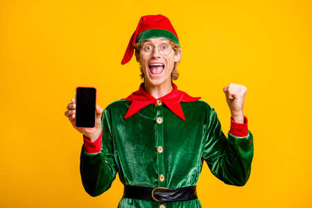 Portrait of his he nice attractive successful glad cheerful cheery funny guy elf holding in hands device rejoicing having fun isolated over bright vivid shine vibrant yellow color backgroundの写真素材