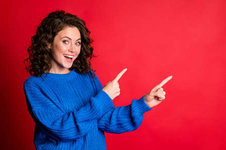 Photo of pretty lovely lady curly hairdo hands direct fingers up empty space open mouth excited surprise positive wear blue knitted sweater isolated red color backgroundの写真素材