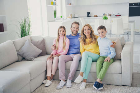 Full body photo of positive family sit couch daddy hug mommy and two kids boy girl in house indoorsの写真素材