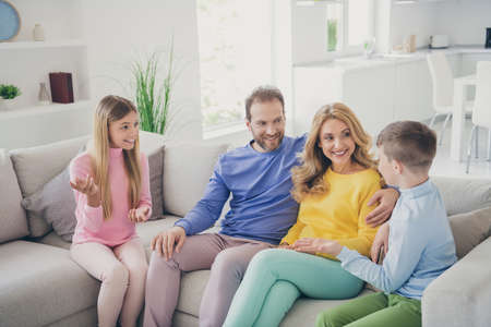 Photo of positive cheerful two kids boy girl sit couch tell mom dad news in house indoorsの写真素材