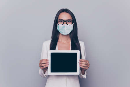 Photo portrait of woman in blue face mask showing tablet with blank space isolated on white colored backgroundの写真素材