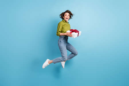 Photo portrait of excited girl jumping up holding red white present in hands isolated on pastel...