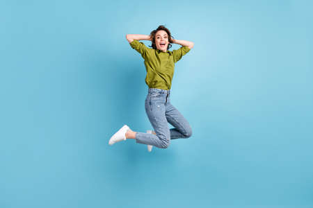 Photo portrait of excited woman jumping up holding head with hands isolated on pastel light blue colored backgroundの写真素材