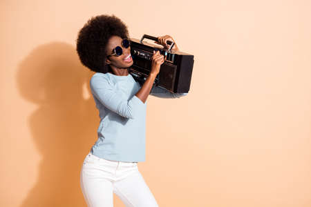Photo portrait of young african american woman regulating volume on boombox isolated on pastel beige...