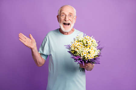 Portrait of friendly cheerful cheery old man holding bunch fresh flowers isolated over violet purple color backgroundの写真素材