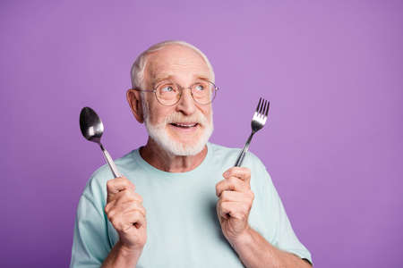 Portrait of funny smiling grandfather hold cutlery looking empty space wear light blue t-shirt...