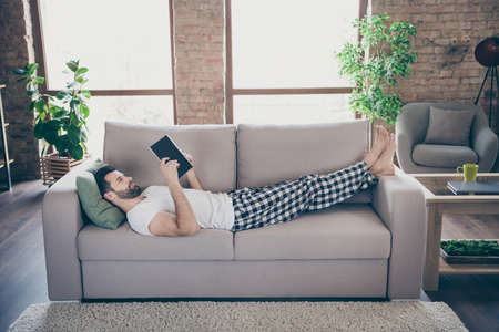 Profile photo of domestic homey handsome guy stay home quarantine reader book worm good mood lying comfy cozy sofa modern interior living room apartments indoorsの写真素材