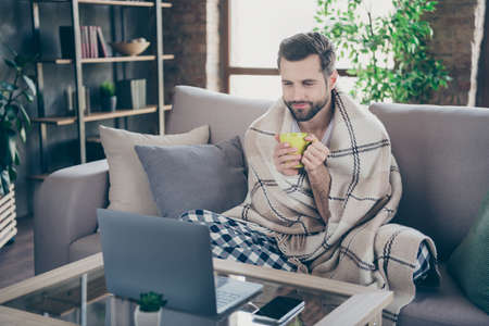 Photo of handsome homey guy sit comfy sofa saturday weekend drink fresh coffee watch film notebook stay home quarantine pajama covered checkered blanket living room indoorsの写真素材