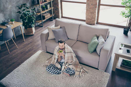 High angle above view photo of handsome guy homey sit comfy floor sofa quarantine stay home eyes closed drink hot tea beverage covered blanket pajama pants t-shirt living room indoorsの写真素材