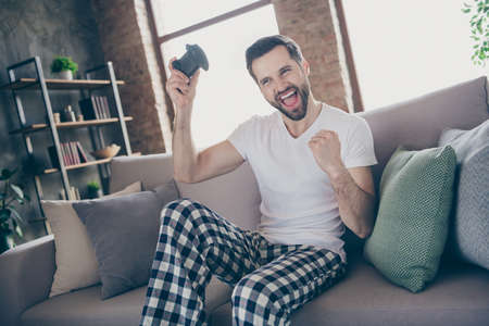 Photo of handsome excited guy homey sit comfy sofa quarantine stay home gamer hold  joystickの写真素材