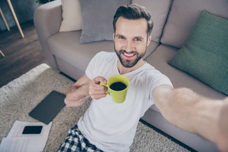 Closeup photo of handsome funny guy sit floor sofa work morning browsing notebook freelancer remote work home quarantine drink coffee take selfies pajama living room indoorsの写真素材
