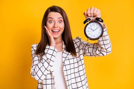 Photo of impressed business woman wear white checkered blazer hold bell arm face cheekbone isolated yellow color backgroundの写真素材