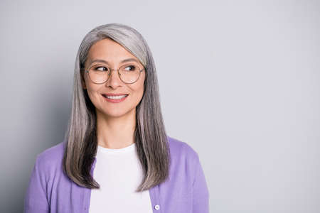 Portrait photo of satisfied smiling senior businesswoman wearing eyeglasses and purple cardigan dreaming planning isolated on grey color backgroundの写真素材