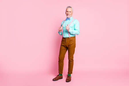 Full length body size portrait of smiling cheerful old gentleman wearing bowtie pants touching suspenders isolated on pink color backgroundの写真素材