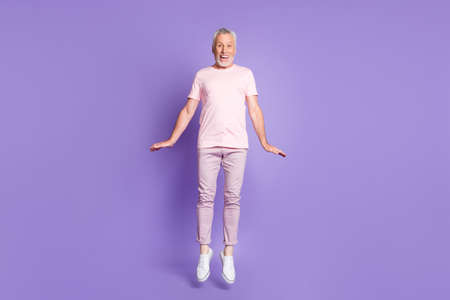 Full length photo of old man jump childish palms wear pink t-shirt trousers sneakers isolated violet color backgroundの写真素材
