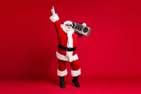 Full body size photo of retired old man grey beard hold boombox shoulder point finger up street dance wear santa costume sunglass headwear leather black boots isolated red color backgroundの写真素材