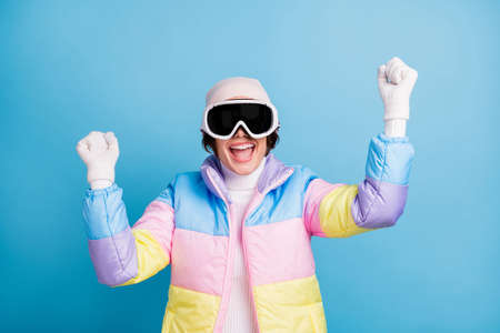 Photo of delighted young woman raise fists excited win wear mask glasses vacation isolated on blue color backgroundの写真素材