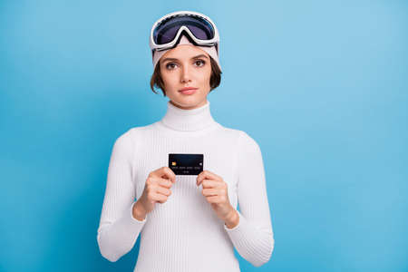 Photo of serious woman hold credit card buy ski gear winter vacation isolated on blue color backgroundの写真素材