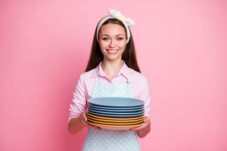Portrait of her she nice attractive pretty lovely cheerful cheery brown-haired housewife holding in hands pile neat clean plates home service done isolated on pink pastel color backgroundの写真素材