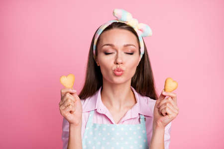 Close-up portrait of her she nice attractive dreamy affectionate brown-haired housewife holding in hands fresh tasty yummy cookies heart form sending air kiss isolated on pink pastel color backgroundの写真素材