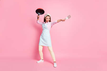 Full size photo of strong chef woman hold frying pan spatula attack enemies wear shirt pants trousers isolated over pastel color backgroundの写真素材