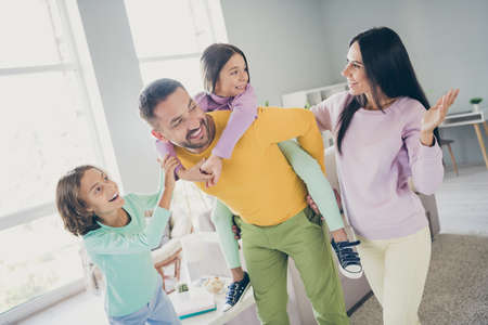 Photo of full family four members talk two small kids daddy hold piggy back daughter wear colorful sweater pants in living room indoorsの写真素材
