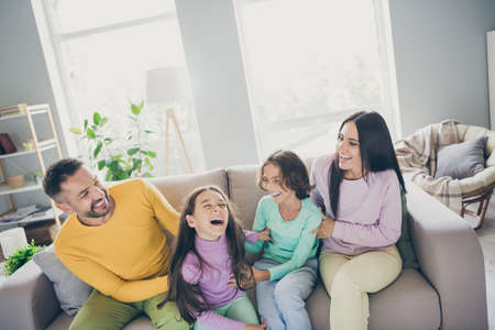 Photo of full big family four members sit couch spend weekend tickling wear colorful pullover trousers in living room indoorsの写真素材