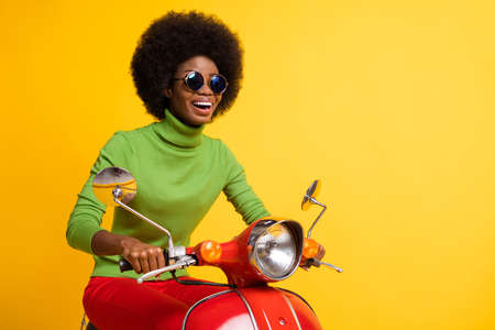 Photo portrait of glad woman on red scooter isolated on vivid yellow colored backgroundの写真素材