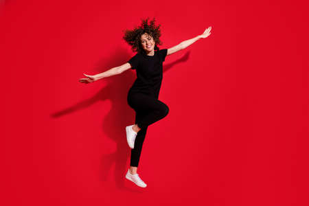 Photo portrait full body view of woman making plane with hands jumping up isolated on vivid red colored backgroundの写真素材
