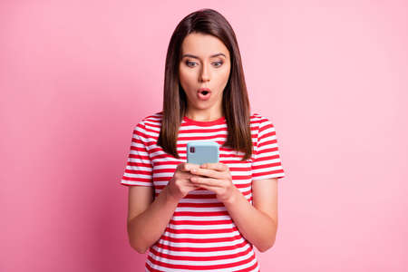 Portrait of impressed young woman staring telephone open mouth wear read white t-shirt isolated over pink backgroundの写真素材