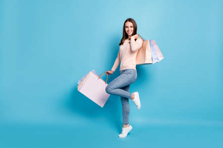 Full length body size view of her she nice attractive cheerful brown-haired girl jumping carrying new things clothes bargain retail outlet isolated bright vivid shine vibrant blue color backgroundの写真素材