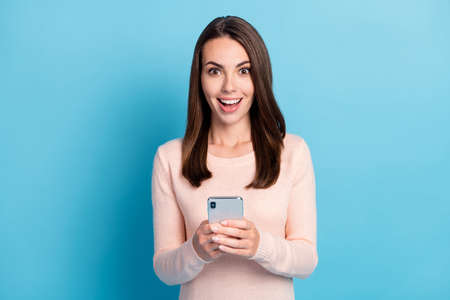 Photo of astonished girl hold smartphone wear pastel beige sweater isolated over blue color...