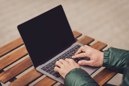 Cropped photo of young guy arms dressed green coat having rest sitting cafeteria typing modern gadget outdoors city streetの写真素材