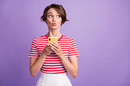 Photo of pretty funny young lady hold cell phone look side empty space wear striped t-shirt isolated...