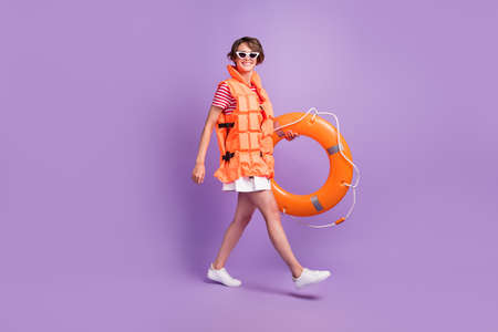 Full length profile photo of girl walk hold rubber ring wear jacket sunglass skirt sneakers isolated violet color backgroundの写真素材