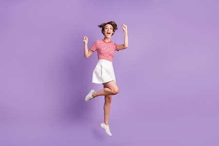 Full length photo of lady jump raise fists open mouth wear striped t-shirt short skirt sneakers...