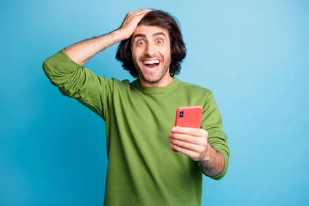 Portrait of handsome guy arm on head unexpected like repost green sweater isolated on blue color...