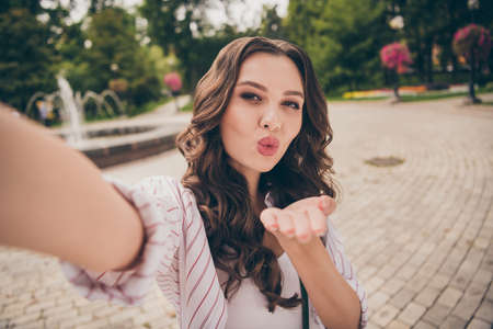 Photo portrait of female blogger with brunette curly hair taking selfie sending air kiss with plump pouted lips wearing casual clothesの写真素材
