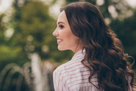 View from bellow of beautiful brunette with curly long hair smiling laughing in green spring city...