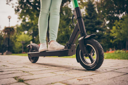 Cropped photo of young woman ride drive electric scooter outside in park sunlight spring timeの写真素材